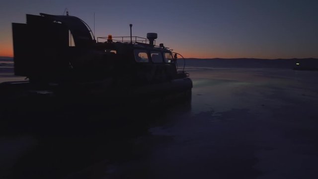 People in hovercraft moving on frozen Lake Baikal against sky during sunset