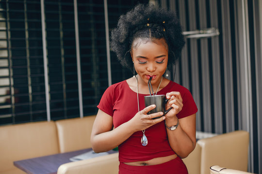 young and beautiful dark-skinned girl with curly dark hair in a red dress standing in a cafe and drinking a coffee