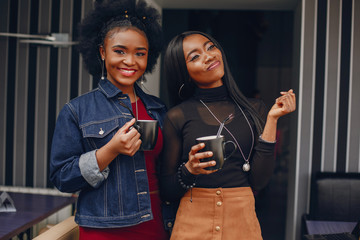 two beautiful and stylish young, dark girls standing in a restaurant and drinking a coffee