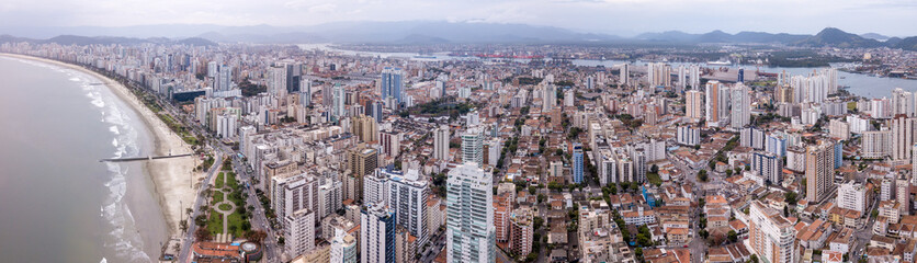 Beautiful aerial drone view of Santos city in Sao Paulo, Brazil. Panoramic Santos skyline with beach, sea, streets and buildings with mountains in the background in foggy day.