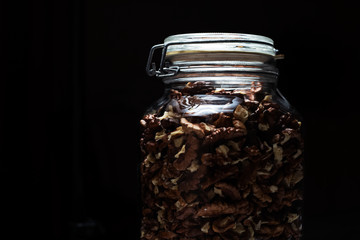 Close-up of glass jar with walnut, on black background.