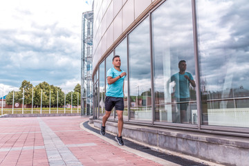sportsman in jump on background of windows, A man runs in summer in city for fitness training sportswear, sneakers, free space for text. Glass building window background. Active lifestyle youth.