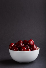Fresh red sweet cherry in white bowl on black background. side view.