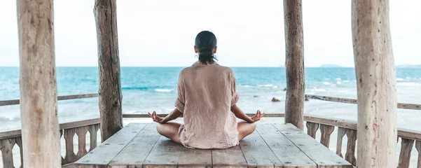 Foto op Plexiglas jonge vrouw die mediteert in een yogahouding op het strand © Natalia