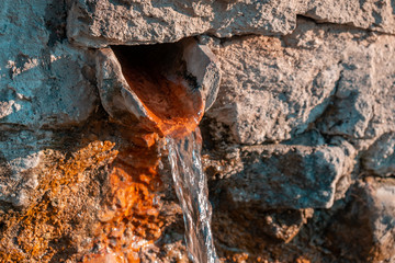 Close up view of a water fountain. Water coming from a hole on the wall covered with algae.