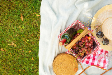 Flat lay Picnic on a green lawn, with a plaid picnic basket and a bottle of wine and glasses, a handbag and a hat with space. Summer mood and outdoor recreation