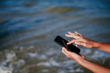 close up view of woman hands holding mobile phone at the beach. Summer and technology concept