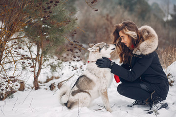 Cute girl in a winter park. Woman palying with a dog. Lady in a black jacket