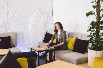 Concentrated at work. Confident young adult middle-aged woman in smart casual clothes, working on a laptop, sitting inside a creative office or cafe. Theme business woman work in free space