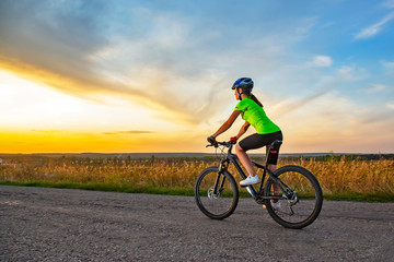 Fototapeta na wymiar Beautiful girl cyclist riding a bike on the road towards the sunset.