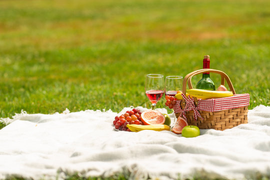 Picnic basket with fruit wine on a bedspread in the garden.