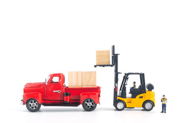Miniature workers model controlling forklift loading cargo on pickup isolated on white background in transportation concept
