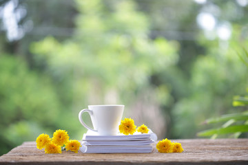 Obraz na płótnie Canvas White coffee cup with yellow Chrysanthemum flowers and notebooks on wooden table at outdoor