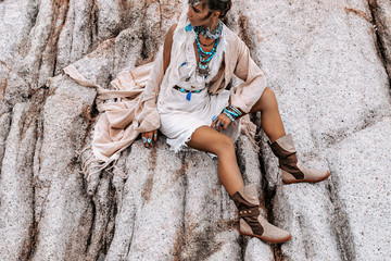 young tribal style woman with lot of boho accessories sitting on a rock