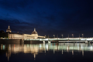 Obraz premium Pont de la Guillotiere bridge in Lyon, France over a panorama of the riverbank of the Rhone river (Quais de Rhone) at night with the main monuments of the old Lyon in background