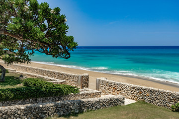 Summer caribbean coastline panoramic view, tropical green garden with stairs to the beach with stone wall, splashes, white Aleli tree, Sosua, Puerto Plata. Dominican Republic