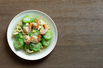 top view of stir fried luffa with shrimp in a ceramic dish on wooden table. delicious and healthy homemade style food concept.