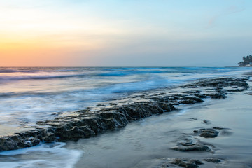 Seascape horizon with rocks in the water and ocean waves at sunrise on Cabarete beach, Dominican Republic