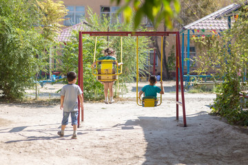 A child swinging on the playground on a sunny summer day in the park. Children's swing. Courtyard of a school or kindergarten and a playground. Little boys fly high in the air on a swing. Kid playing