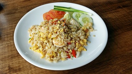 Seafood fried rice with tomato slices, cucumber slices and scallion in white plate on wooden table.