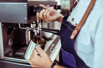 Barista steaming milk in the pitcher with coffee machine preparing to make latte art in cafe, Coffee machine in steam, barista preparing coffee at cafe