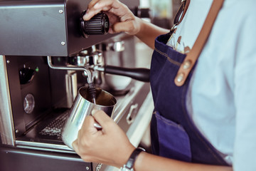 Barista steaming milk in the pitcher with coffee machine preparing to make latte art in cafe, Coffee machine in steam, barista preparing coffee at cafe
