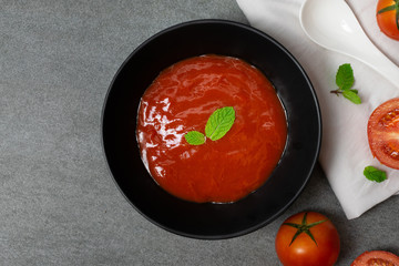 Tomato sauce and mint leaves in black bowl with tomatoes sliced on concrete table.