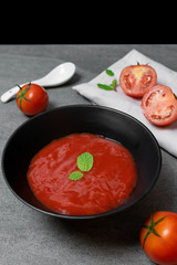 Tomato sauce and mint leaves in black bowl with tomatoes sliced on concrete table.
