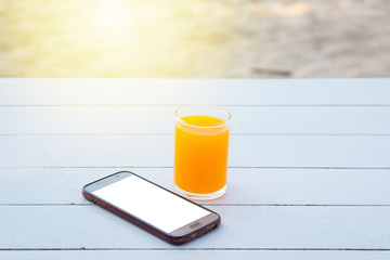 Orange juice in glass and mobile phone on white wooden table