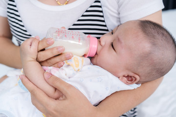 baby drinking milk from baby bottle with mother