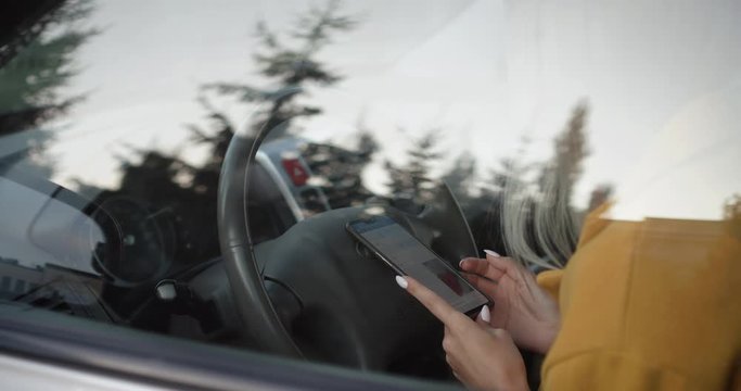 Close-up hands young woman using her smartphone at the wheel of a car. Communication in social networks.