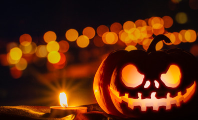 Spooky pumpkin head jack o' lantern glowing with a burning candle. Halloween background, bokeh