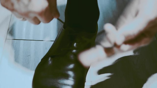 A stylish handsome man is tying up the shoue-laces on his expensive black leather shoes.
