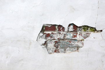 Old white wall in cracks with red brick. Urban texture. Old red brick wall with damaged white plaster. Plastered brick wall, rough background. Loose plaster.