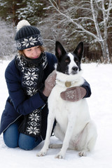 Portrait of beautiful young woman with her black and white dog on a background of winter snowy forest.