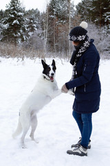 Portrait of beautiful young woman with her black and white dog on a background of winter snowy forest.