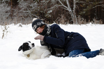 Portrait of beautiful young woman with her black and white dog on a background of winter snowy forest.