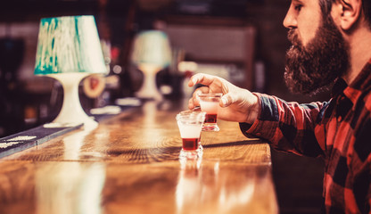 Tequila shots, vodka,whisky, rum. Drinking alcohol into shot glasses in a nightclub or bar. Barman in pub. Bearded man in pab. Bearded man shots cocktail. Tequila shot. Colorful cocktails at the bar