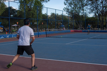 Obraz premium Hombre adulto latino de camiseta blanca en pantaloneta negra jugando tenis con amigo en cancha profesional hispano