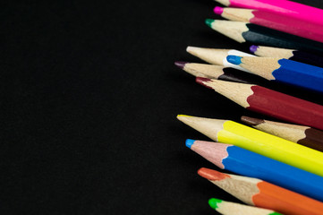 Many colorful pencils lie on a black background paper