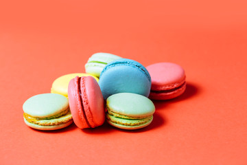 Close up of sweet green, yellow, coral, blue macaroons on red background. Fresh pastries, Breakfast, cafe