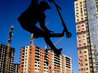 Silhouette of a man on a scooter. In the background, high-rise buildings under construction