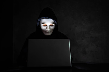 Male hacker hidden face with the mask accessing to personal information on laptop in the dark. Technology, cyber crime concept. Space for text.