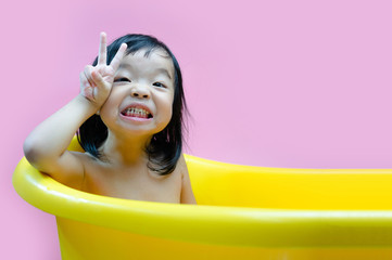 Three year old kid bathed in a yellow basin and playing with camera. Soap bubbles and kid bathing.