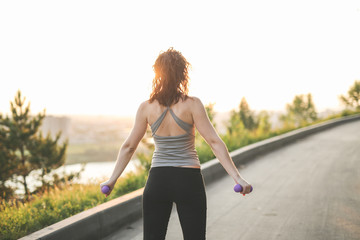 woman with dumbbells goes in sports in park