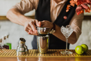 A photo of man's hands squeezing lime juice into a shaker at the bar. Selective focus, natural light.