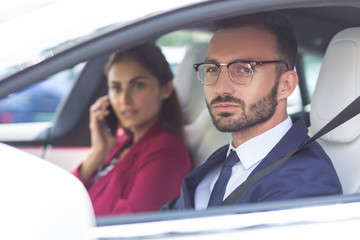 Bearded husband driving car while wife speaking by phone
