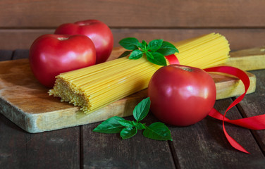 Bunch of raw spaghetti pasta, red ripe tomatoes and green basil leaves. Selective focus.