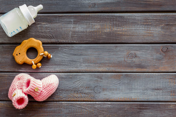 Pink knitted footwear and rattle, bottle for baby on wooden background top view mockup