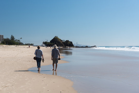 A baby boomer couple walking along Tugun Beach towards Elephant Rock. On the Gold Coast, Queensland, Australia.
